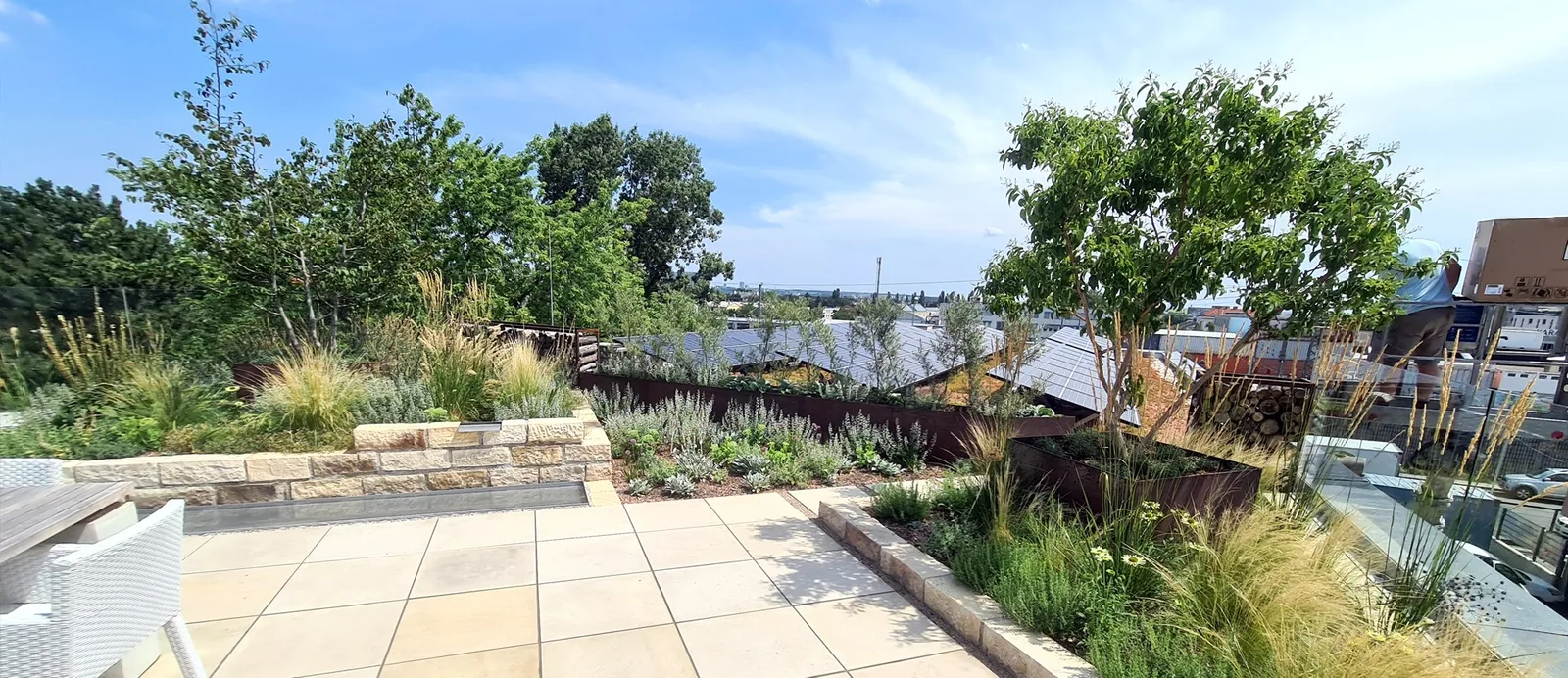 Begrünte Dachterrasse mit Steinplatten, Beeten und Blick über die Stadt