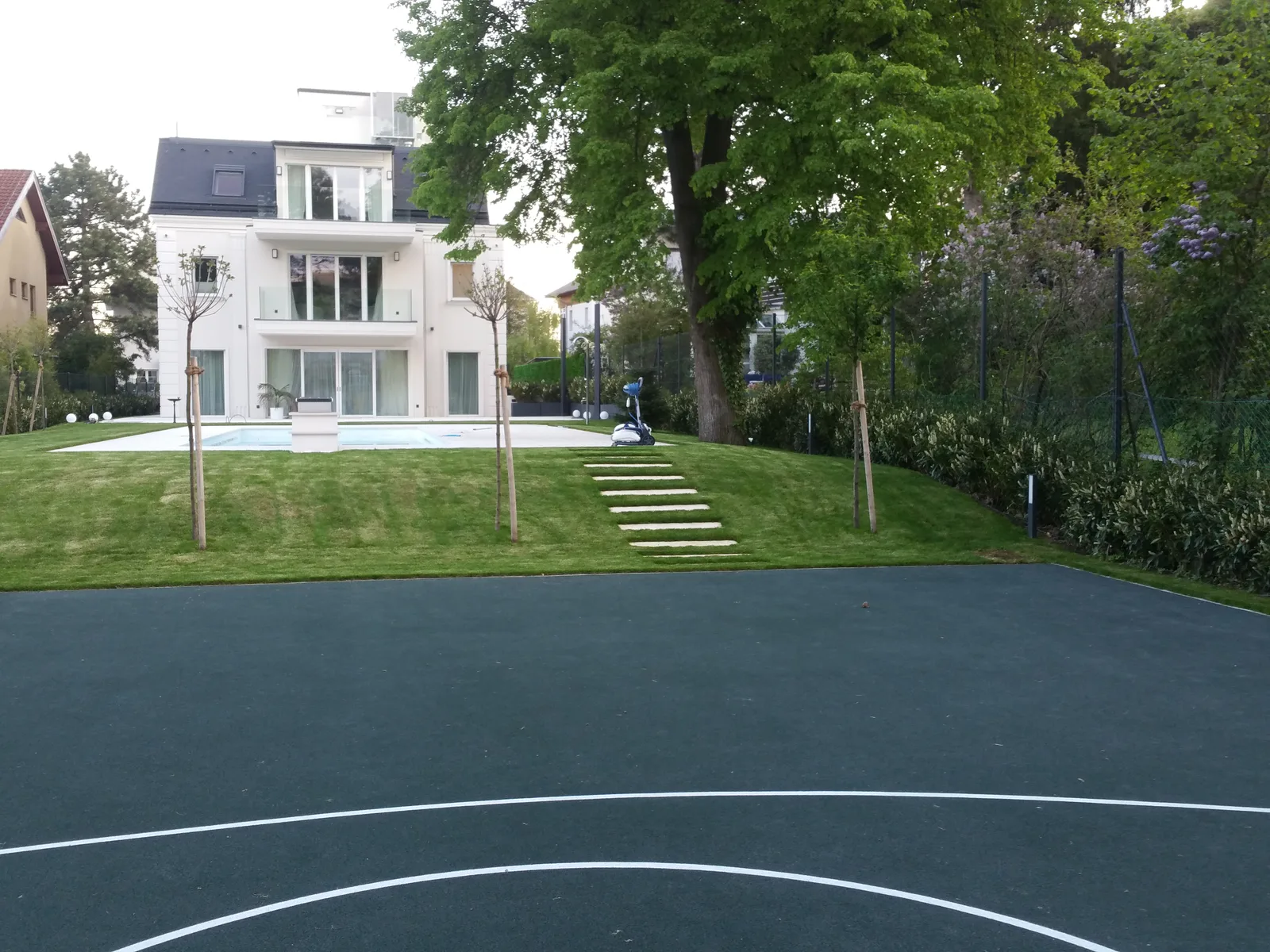 Garten mit Rasenhang, Trittplatten, Pool und Basketballplatz vor einer Villa