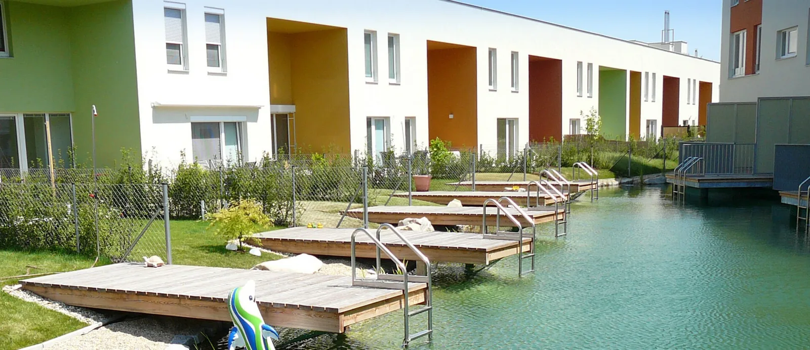 Schwimmteich zwischen Reihenhäusern mit Holzstegen ins Wasser