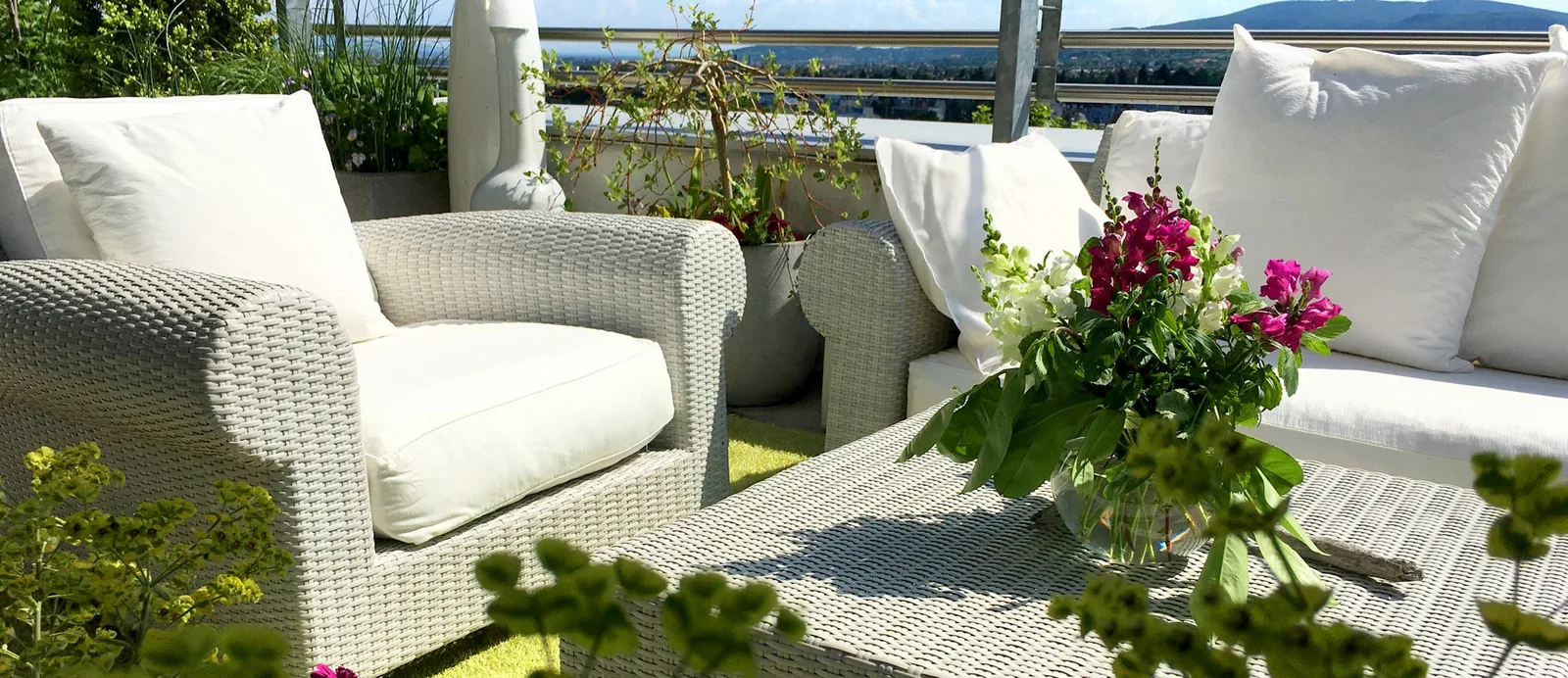 Dachterrasse mit weißen Loungemöbeln und einem Blumenstrauß